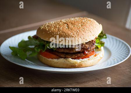 Homemade double hamburger with lettuce and tomato in a white plate on the dining table Stock Photo