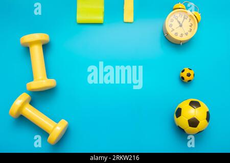 Yellow sports items: dumbbells, balls, elastic bands for sports, alarm clock, on a blue background Stock Photo