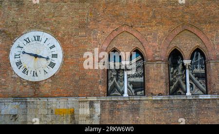 Old clock on exterior brick wall of Santa Maria della Scala, Siena. Tuscany, Italy Stock Photo
