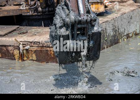 Dredging the bottom of water area, view of the bucket of the floating excavator full of mud Stock Photo