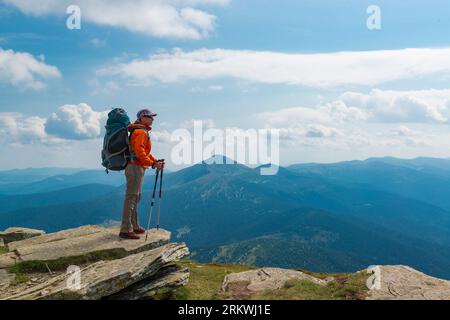 Hiker woman with backpack and trekking poles on the mountain top. Active lifestyle and outdoor vacation in the mountains Stock Photo