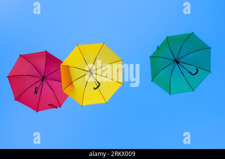 Three colorful umbrellas - red, yellow and green - fly in the blue sky Stock Photo