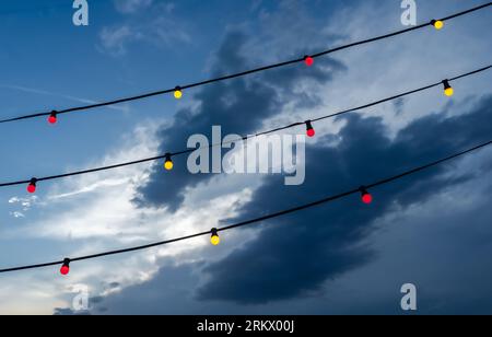 Red and yellow electric lights on cables and a dramatic sky with dark clouds in the background Stock Photo