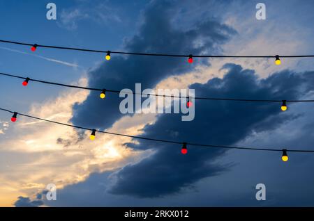 Red and yellow electric lights on cables and a dramatic sky with dark clouds in the background Stock Photo