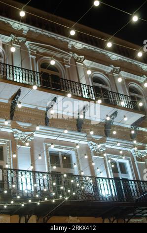 Historic building exterior in classical style. White and beige, tall windows, balcony with black metall railing. Decorative bulbs, lighting, illuminat Stock Photo