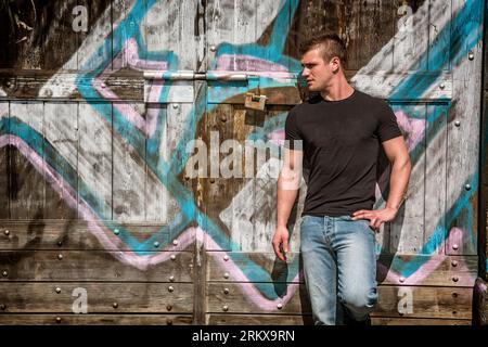 Photo of a man leaning against a graffiti-covered wall Stock Photo