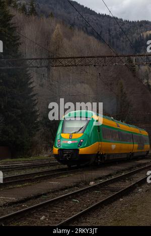 Train passing through the forest.Yellow and green train, railway in mountains Stock Photo