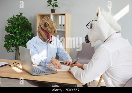 Two businessmen in dinosaur and horse animal masks signing paper document at meeting Stock Photo