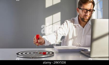 Business man holding dart on target to successful goal at the desk in office. Stock Photo