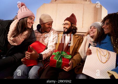 Smiling multiracial group people sitting holding present winter christmas gifts. Happy young friends Stock Photo