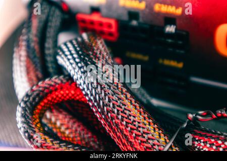 Wiring on power supply of desktop PC close-up with selective focus. Computer cables hardware components background in red color light Stock Photo