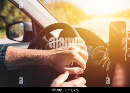 Man with both hands on steering wheel driving at sunset Stock Photo