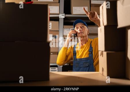 Old man worker talking on a mobile phone to checking inventory in the warehouse store Stock Photo