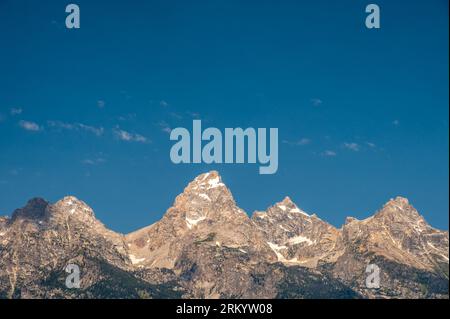 Grand Tetons Stand Bright Against Blue Sky and Sparse Clouds in Wyoming Stock Photo