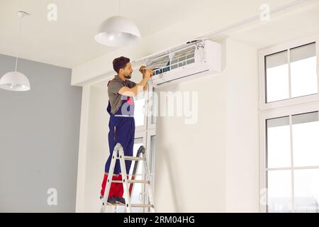 Technician standing on ladder installing or fixing modern air conditioner on white wall Stock Photo