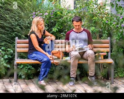 Young couple eating light lunch sitting on park bench in city center - Tours, Indre-et-Loire (37), France. Stock Photo