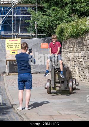 Parent taking photo of son sitting on old canon barrel, Castle Hill, Lincoln City, Lincolnshire, England, UK Stock Photo