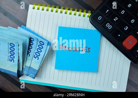 Concept of Priorities write on sticky notes isolated on Wooden Table. Stock Photo