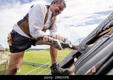 Roofer in traditional gear working on roof using saw Stock Photo