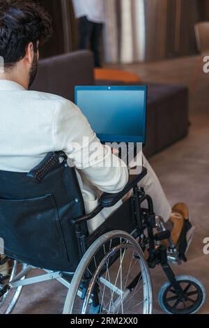 Disabled employee in wheelchair working on lap top. Back view shot Stock Photo