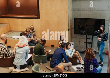 Caucasian businesswoman giving speech to diverse young entrepreneurs, using presentation monitor, graph charts, statistics Stock Photo