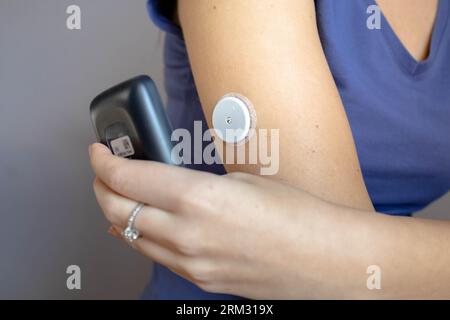 Female hand with continuous glucose monitor doing reading from the arm patch Stock Photo