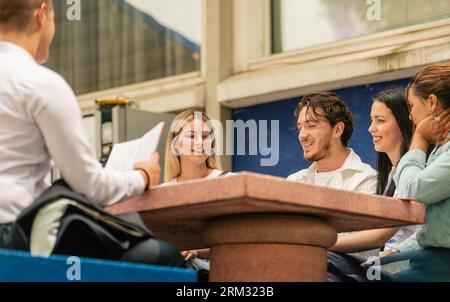 Group of young classmates sitting, talking and laughing outside Stock Photo