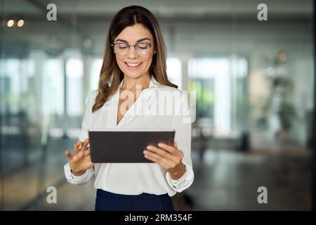 Smiling mid aged professional business woman holding tablet in office. Stock Photo