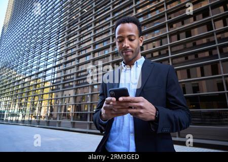 Young adult latino male outside modern office building using phone. Business man in formal clothes. Stock Photo