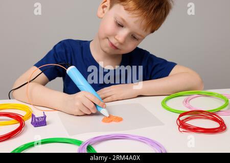 Boy drawing with stylish 3D pen at white table Stock Photo