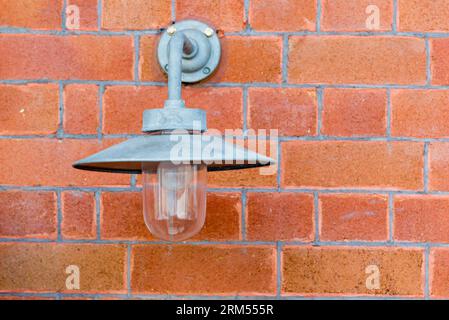 An older style outdoor or outside light mounted on a brick wall in Sydney, Australia with a tin hat style shade to reduce upward spread of light Stock Photo