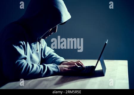 Male hacker writing code on a laptop Stock Photo