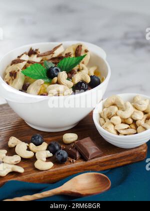 Healthy healthy breakfast. Fruit salad with banana, cashew, blueberry, chocolate and corn flakes. Fitness recipe for healthy balanced breakfast. Still life. Top view. Stock Photo