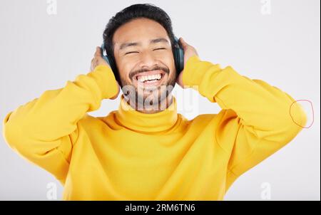 Man, headphones and excited for listening in studio, smile or hearing with streaming subscription by white background. Indian guy, student or fashion Stock Photo