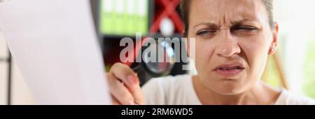 Incredulous middle age woman looking on document trough magnifying glass close-up. Stock Photo