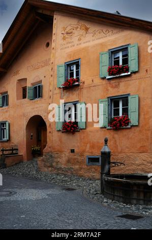 Facade of traditional Swiss house, renovated in 1997, in Guarda, a mainly Romansch-speaking village in the Lower Engadin Valley in Graubünden or Grisons canton, Switzerland.  It is decorated with Romansch inscriptions and an image of a long-armed “dragun” (top right). Stock Photo