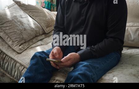 man sitting on sofa and looking at smartphone Stock Photo