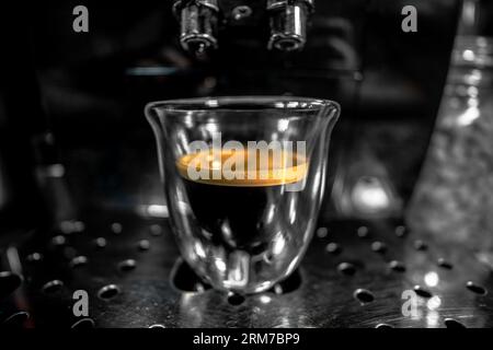 Glass cup with freshly brewed black coffee with foam and golden cream with bubbles visible through the transparency of the cup from a fully automatic Stock Photo