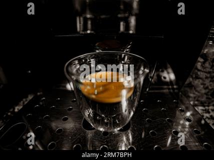 Glass cup with freshly brewed black coffee with foam and golden cream with bubbles visible through the transparency of the cup of a fully automatic es Stock Photo