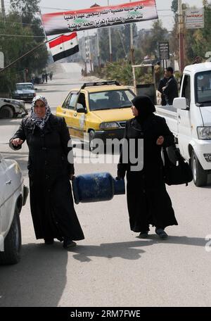 (140302) -- DAMASCUS, March 2, 2014 (Xinhua) -- Syrian women carrying a gas cylinder come back into al-Moadamiya, a district on the outskirts of Damascus that has been besieged by the government troops for months, in Syria, March 2, 2014. Over the past few weeks, some rebel-held areas have accepted what the government calls national reconciliation deals, whereby they surrender their weapons, or agree to truces, in exchange for allowing food to enter and people to leave. Many refugees have come back to their home after that deal.(Xinhua/Bassem Tellawi)(zhf) SYRIA-DAMASCUS-RECONCILIATION PUBLICA Stock Photo