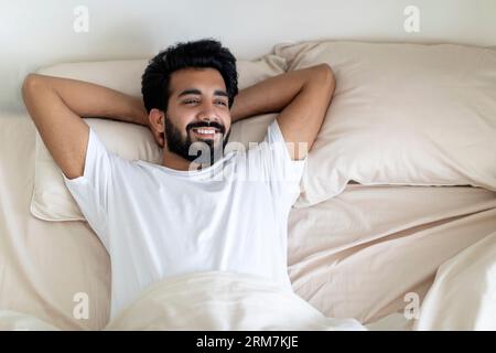 Morning Relax. Smiling Indian Man Lying In Comfortable Bed After Waking Up Stock Photo
