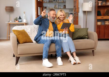 Senior Couple Making Video Call Via Tablet Waving Hand Indoors Stock Photo