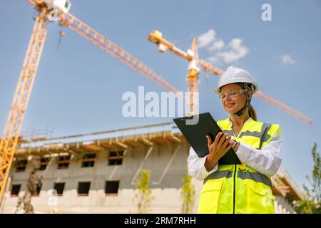 Professional female engineer in protective helmet making notes on construction site Stock Photo