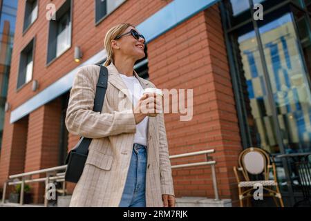 Smiling business woman drinking coffee during break time near office building Stock Photo