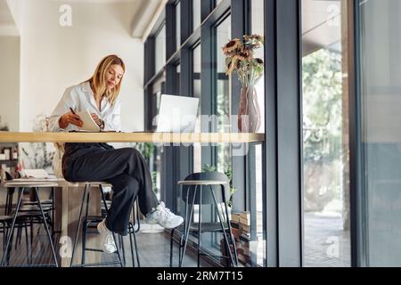 Smiling business woman working on laptop, making notes in cozy coworkign space interior Stock Photo