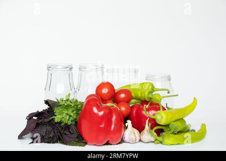 Peppers, garlic, tomatoes, hot peppers and jars lie on a white background, prepare ingredients for adjika, vegetables Stock Photo