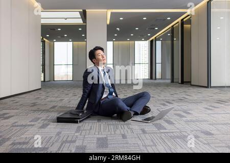 Businessman sitting on floor in empty office Stock Photo