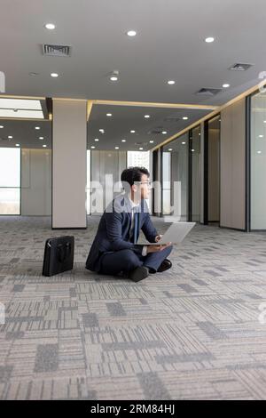 Businessman using laptop on floor in empty office Stock Photo