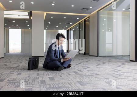Businessman using laptop on floor in empty office Stock Photo