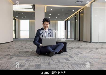 Businessman using laptop on floor in empty office Stock Photo